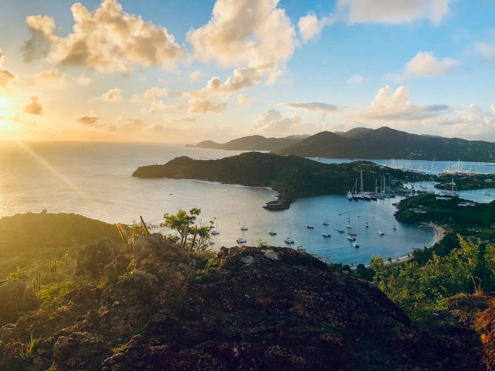 Sailboats anchored in a bay surrounded by green hills under a golden sky