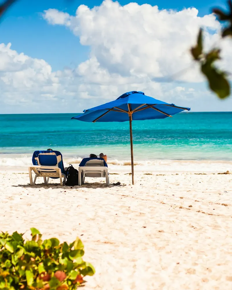a couple of lawn chairs sitting on top of a sandy beach