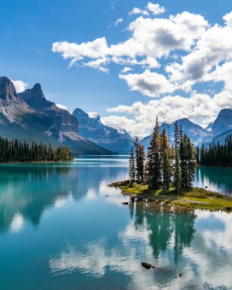 green trees near lake and mountains under blue sky during daytime