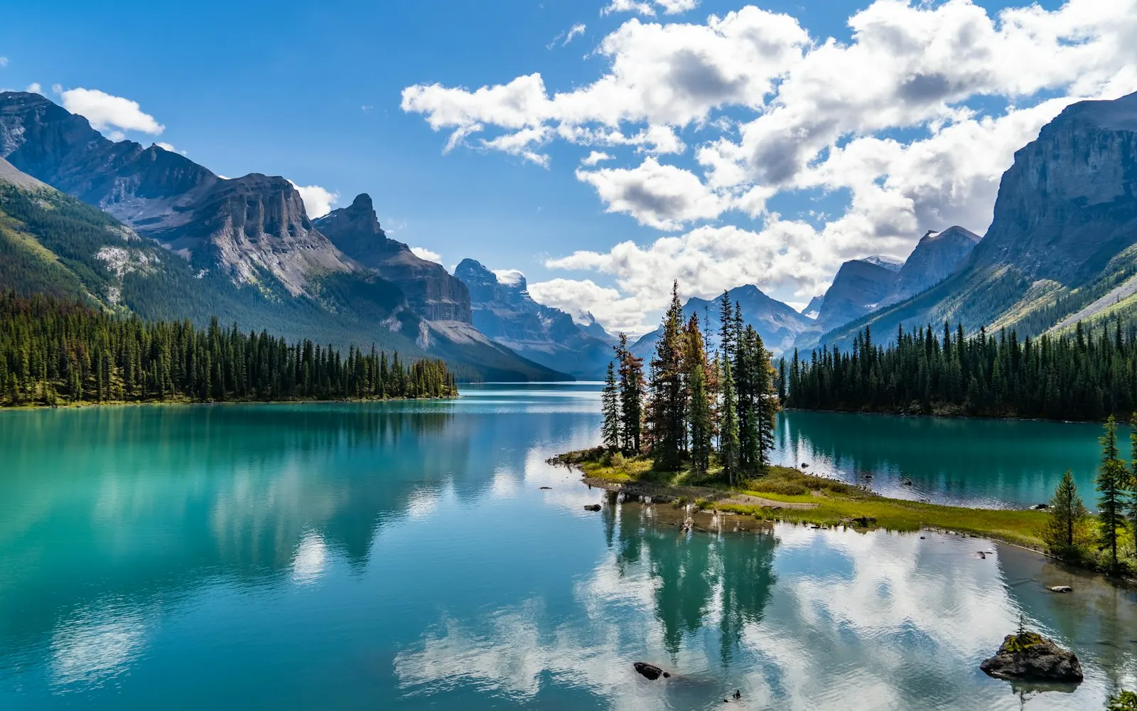 green trees near lake and mountains under blue sky during daytime