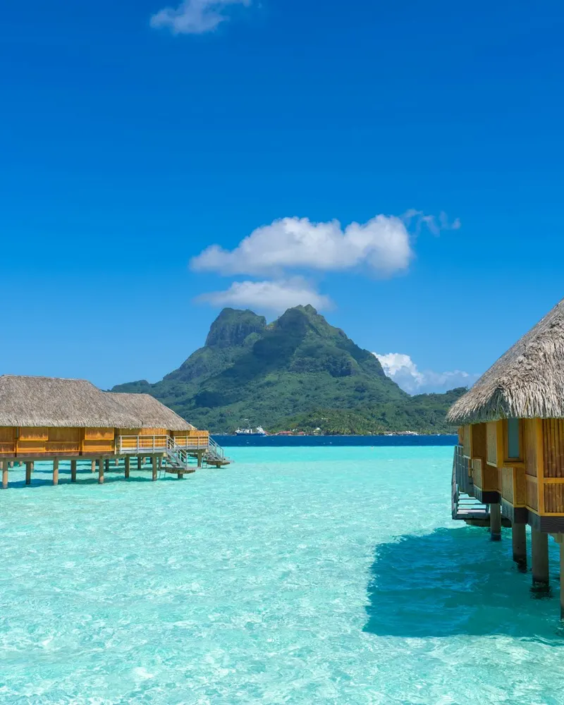The water is crystal blue and clear and there are huts in the water
