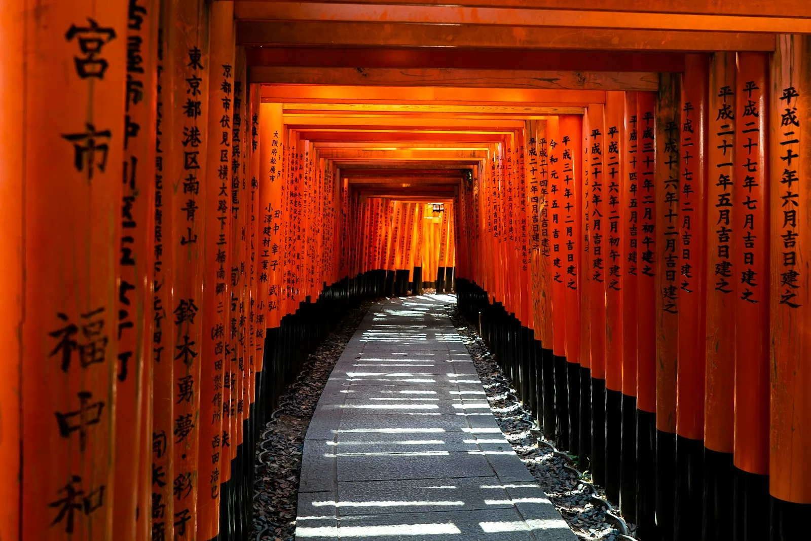 A stone path through a tunnel of orange torii gates in Kyoto, Japan