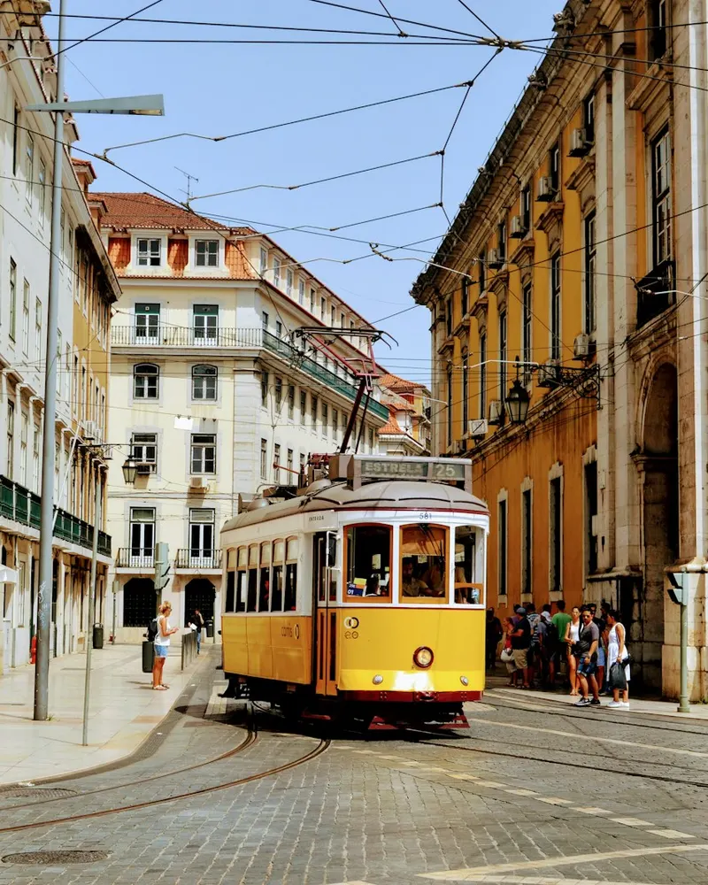 A yellow tram traveling through a street lined with historic buildings in Lisbon, Portugal