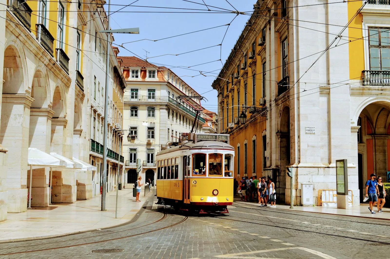 A yellow tram traveling through a street lined with historic buildings in Lisbon, Portugal