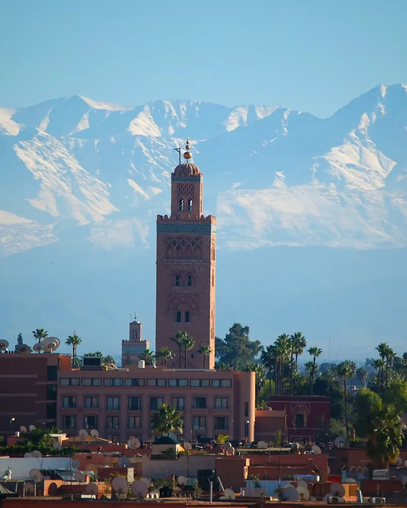 The Koutoubia Mosque minaret rising above Marrakesh with snow-capped Atlas Mountains in the background