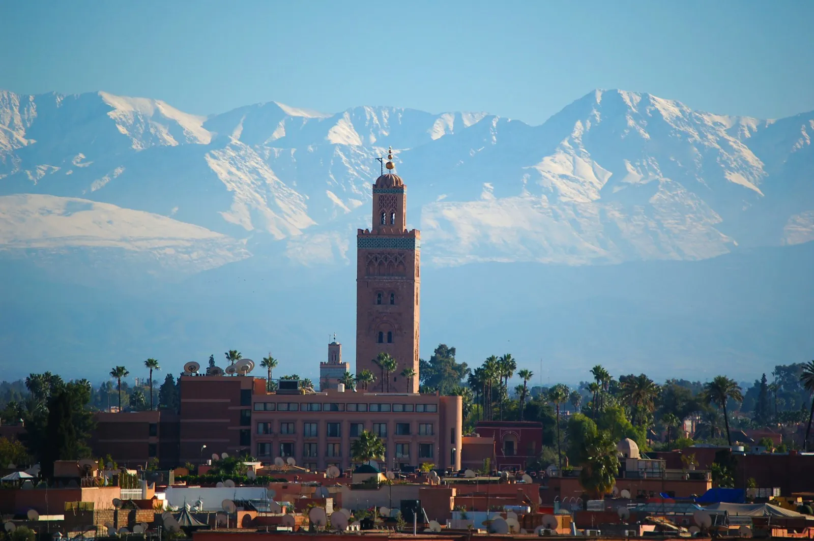The Koutoubia Mosque minaret rising above Marrakesh with snow-capped Atlas Mountains in the background