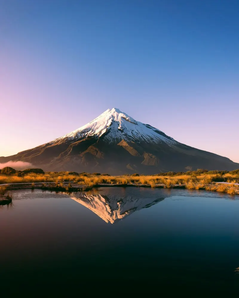 Mount Taranaki reflected in the Pouaki Tarns under a clear sky at golden hour