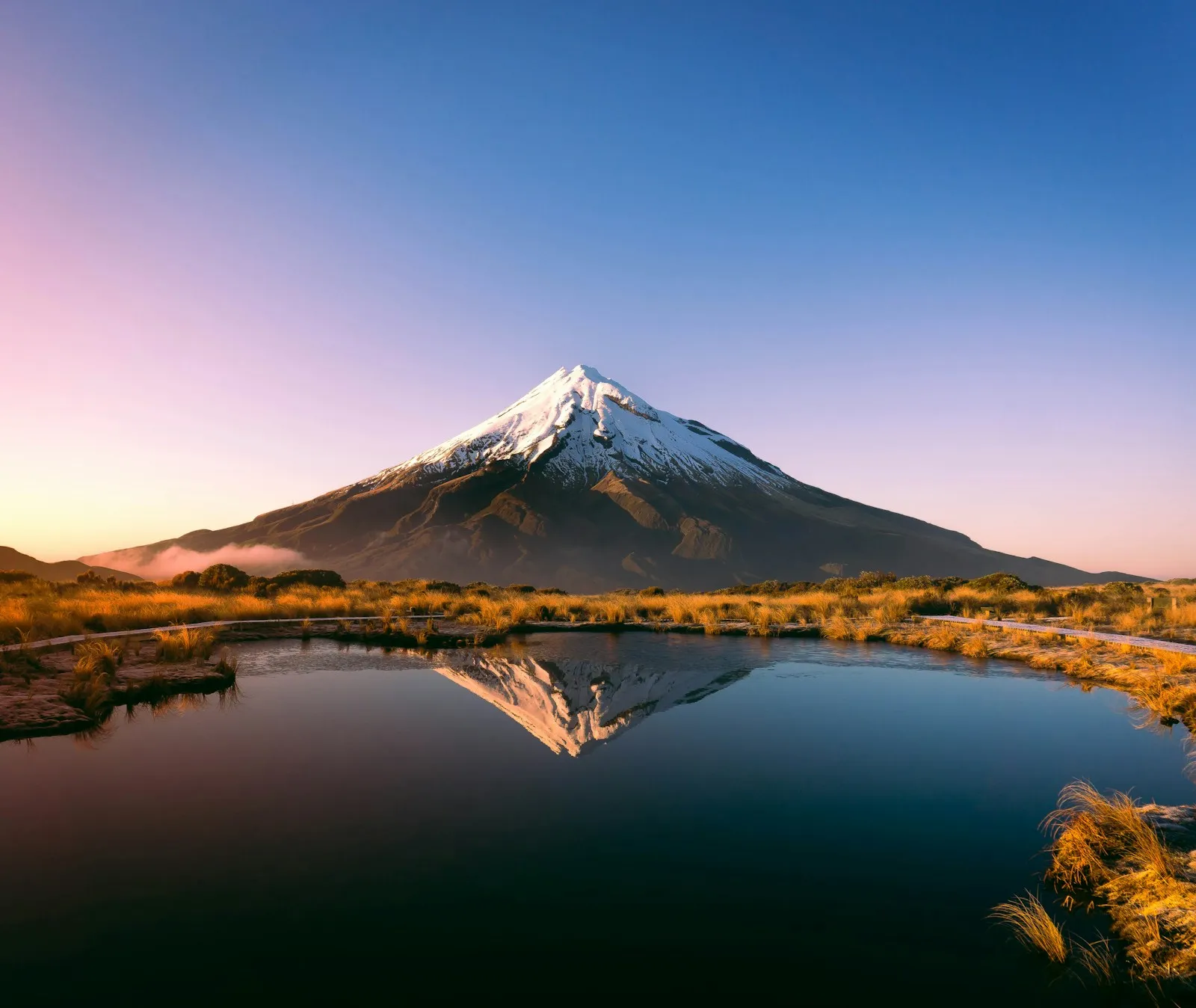 Mount Taranaki reflected in the Pouaki Tarns under a clear sky at golden hour