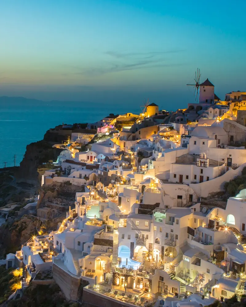 White buildings on a cliffside in Oia, Greece, illuminated by warm evening light